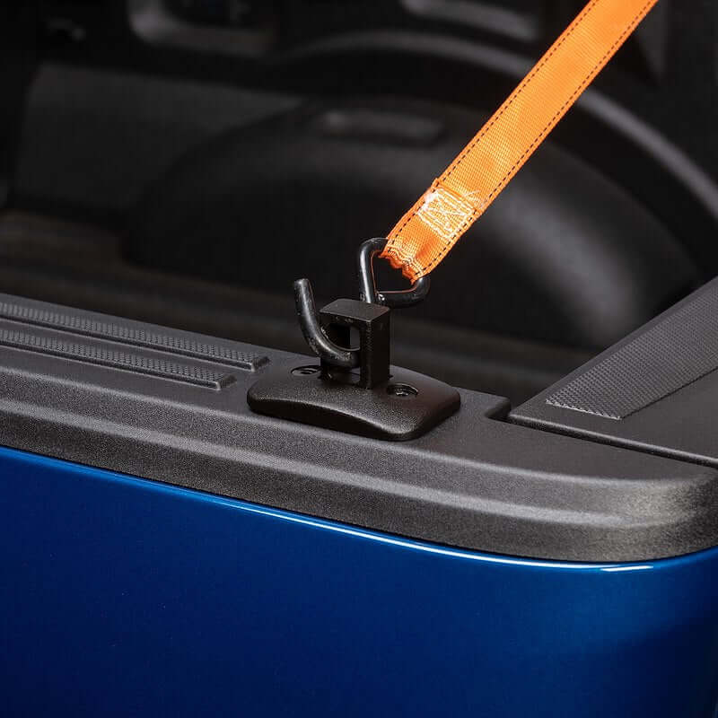 Close-up of Putco Black Tie-Down Anchor in a pickup truck bed, securing cargo with an orange strap.