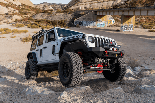 White Jeep Wrangler JL with black flat fender flares and large off-road tires parked on rocky desert ground