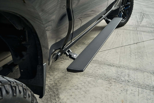 Black power running board deployed beside a black pickup truck, one of the best truck running boards for tall trucks