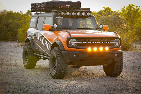 Orange Ford Bronco with a rooftop tent, a row of LED lights on the roof rack and amber lights on the front bumper