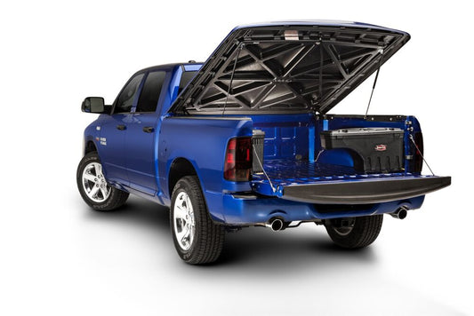 Blue pickup with its hard tonneau cover raised, showing a swing-out toolbox mounted at the side of the truck bed
